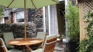 A patio with a round wooden table and four chairs, an umbrella, and a stone wall backdrop.