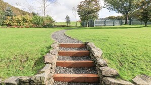 A pathway leading to a wooden deck with a stone wall on one side. - Foresters Cottage (Ulverston)