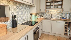 A kitchen with white cabinets, a black coffee machine, a sink, and a patterned backsplash. - Foresters Cottage (Ulverston)