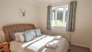 A neatly made bed with a patterned bedspread, a headboard, and a bedside table with a lamp. - Foresters Cottage (Ulverston)