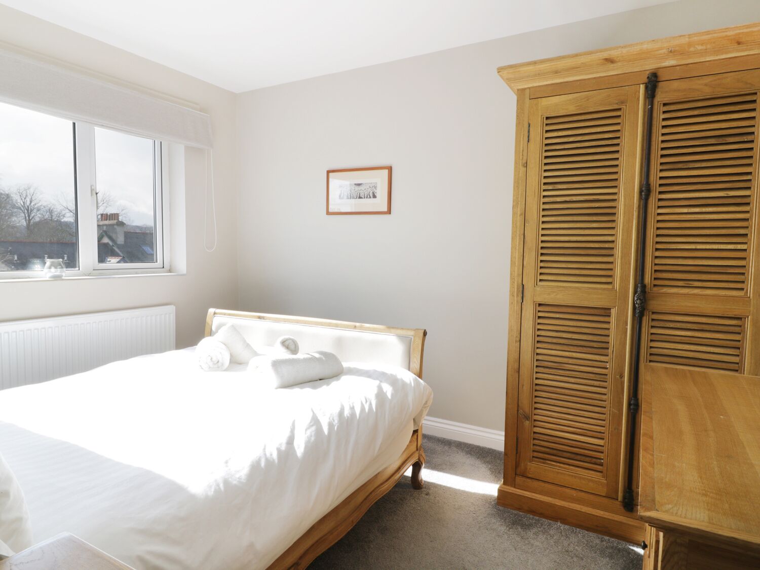 Un dormitorio con una cama, una ventana, un radiador y un armario de madera.