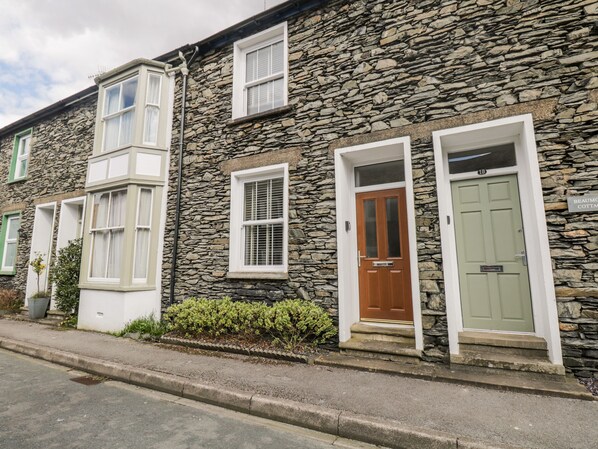 A stone-built cottage with a green door, a white-framed window, and a sign indicating the property name. - Raglan Cottage (Windermere)
