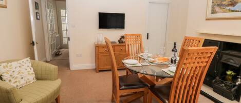A dining area with a glass table, wooden chairs, and a television above.