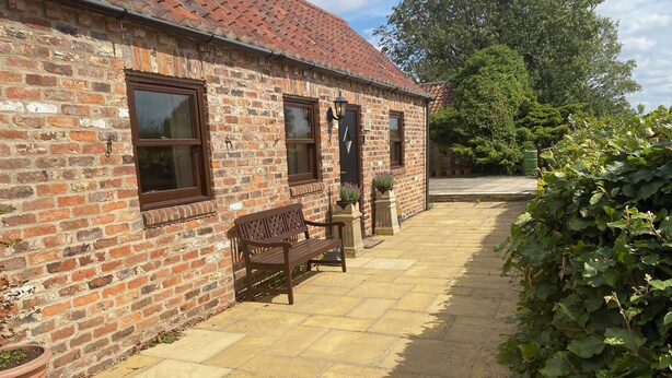 A brick building with a tiled patio, a bench, and potted plants.