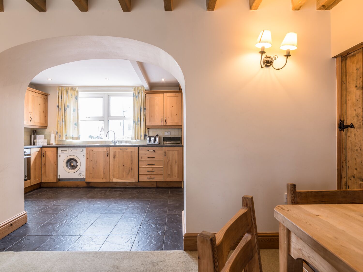 A kitchen with wooden cabinets, a washing machine, and a dining area with a table and chairs.