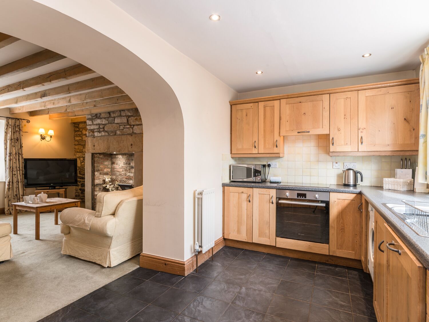 A kitchen with wooden cabinets, a built-in oven, and a microwave. There is a stone wall and a fireplace in the background.
