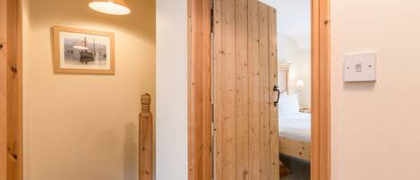 Un couloir avec une porte en bois, un tableau encadré au mur et un luminaire au plafond.