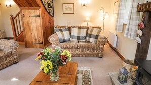 Uma sala de estar aconchegante com escada de madeira, sofá estampado, mesa de centro de madeira com um vaso de flores e lareira.
