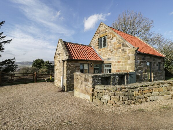 A stone house with a red-tiled roof, a gravel driveway, and a stone wall. - The Piggery (Whitby)