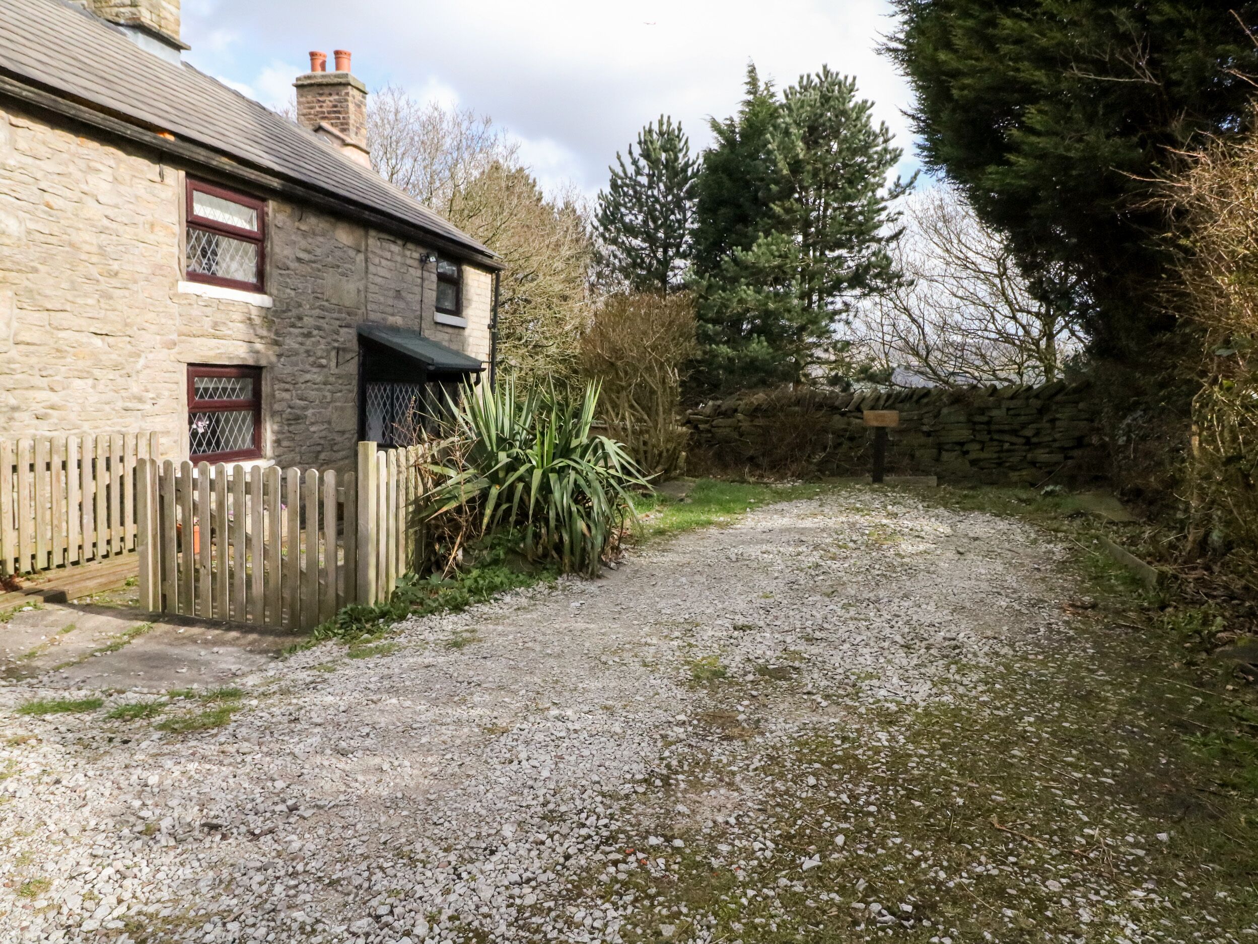 A stone house with a gravel driveway, wooden fence, and a stone wall.