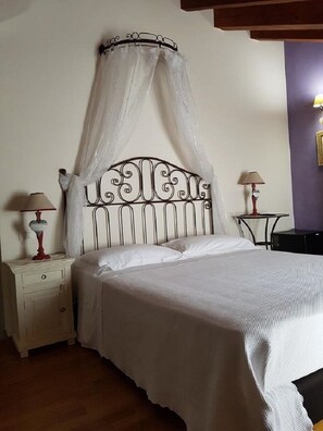 A neatly made bed with a canopy, two bedside tables with lamps, and a small table with a lamp. - Affittacamere La Collina Degli Ulivi (La Spezia)
