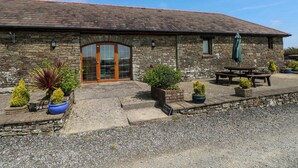 A stone building with a tiled roof, a glass door entrance, and outdoor seating. - The Dairy (Swansea)