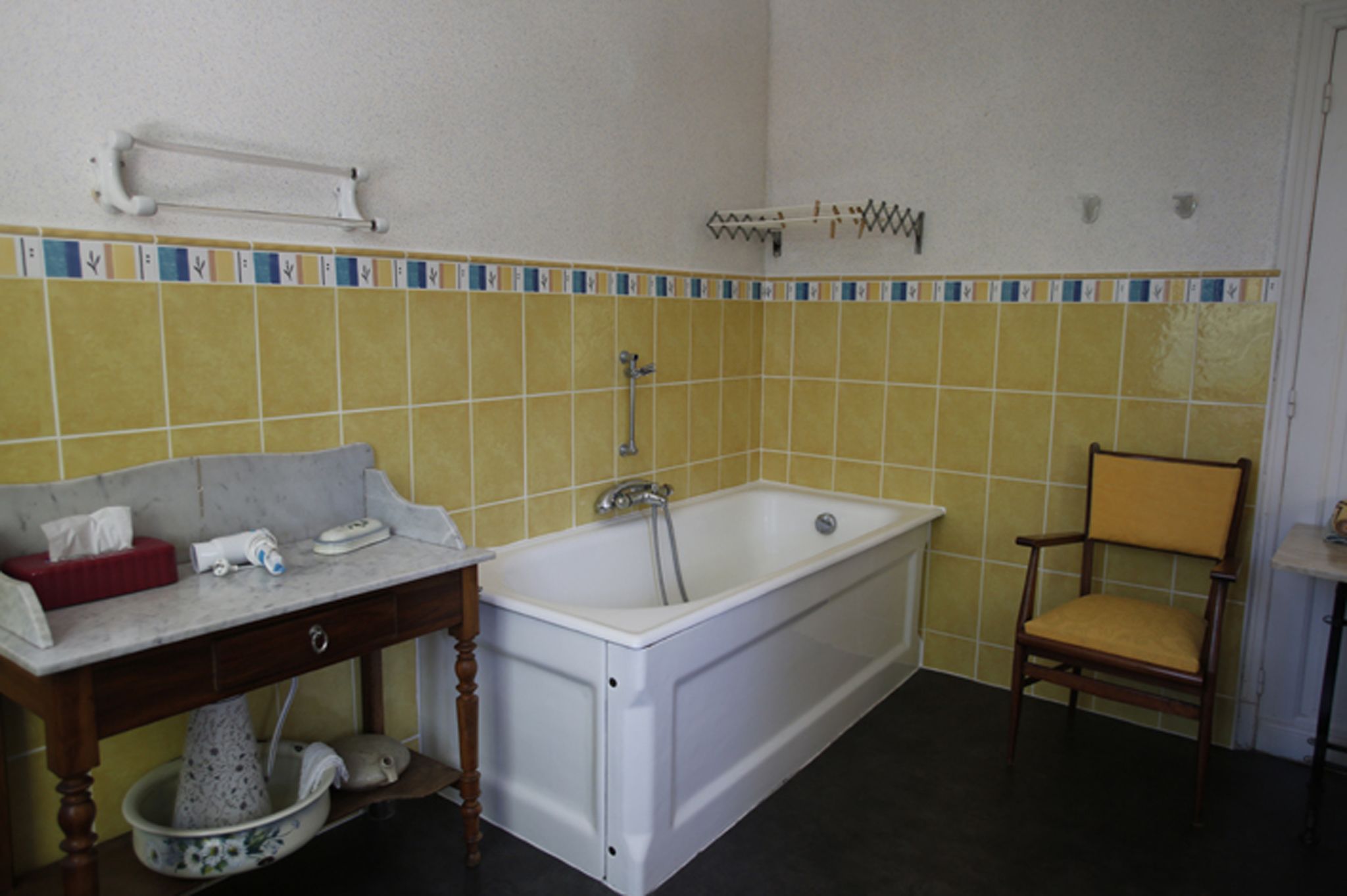 Ein Badezimmer mit Badewanne, einem Holzstuhl, einem Waschbecken mit Spiegel und einem Handtuchhalter.