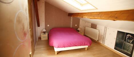 A bedroom with a skylight, wooden floor, and a bed with a pink bedspread.