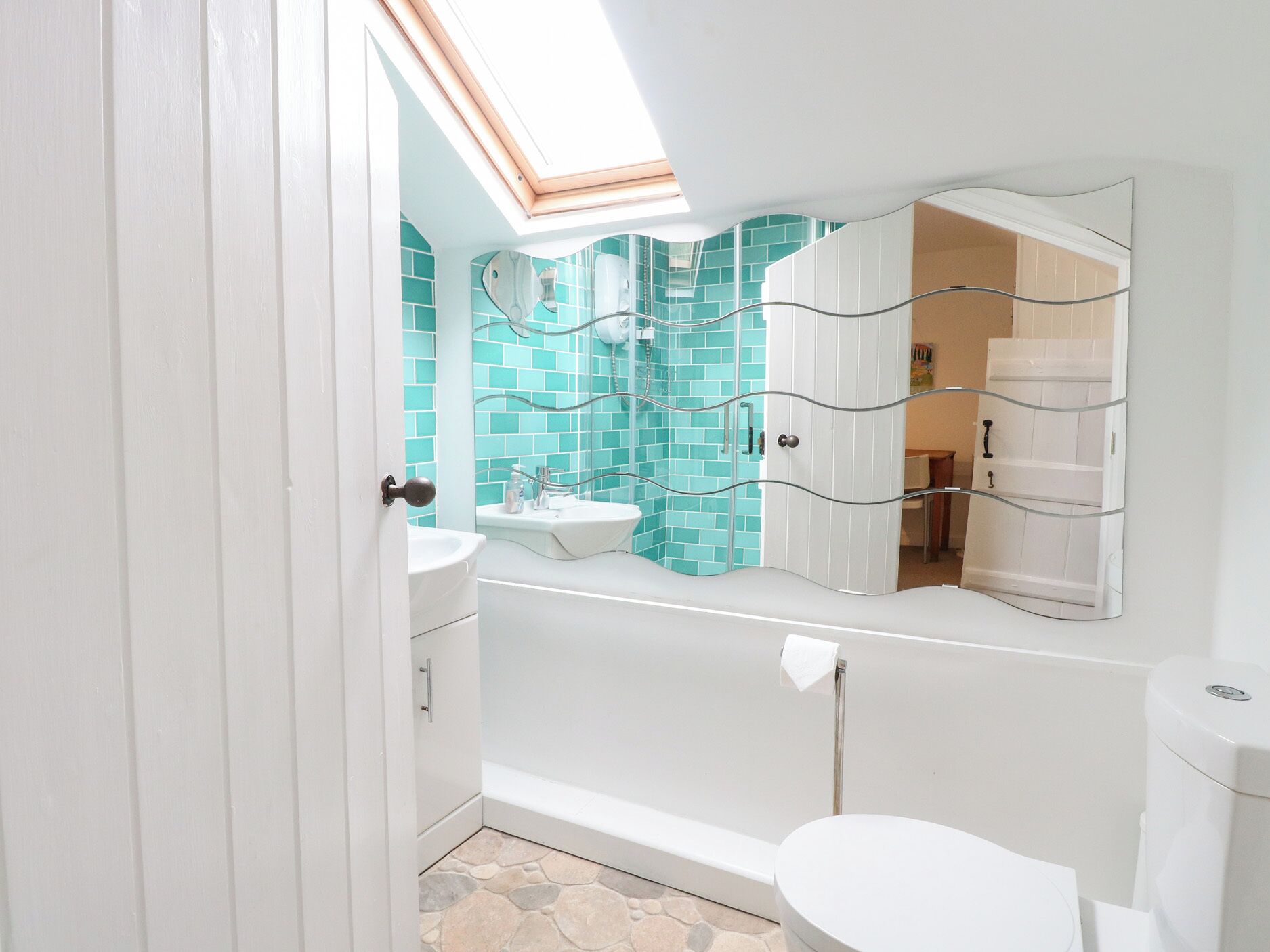 A bathroom with a skylight, a white sink, a mirror, and a toilet.
