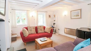 A cozy living room with a red sofa, a wooden coffee table, and a purple sofa. There is a white ladder against the wall and a framed picture on the wall. - Broom Cottage (King's Lynn)