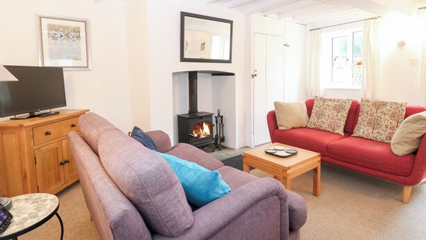 A cozy living room with a sofa, a television, a small table, and a wood-burning stove. - Broom Cottage (King's Lynn)