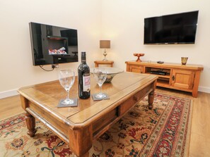 A wooden dining table with two wine glasses and a bottle of wine. A flat-screen TV is mounted on the wall above the table.