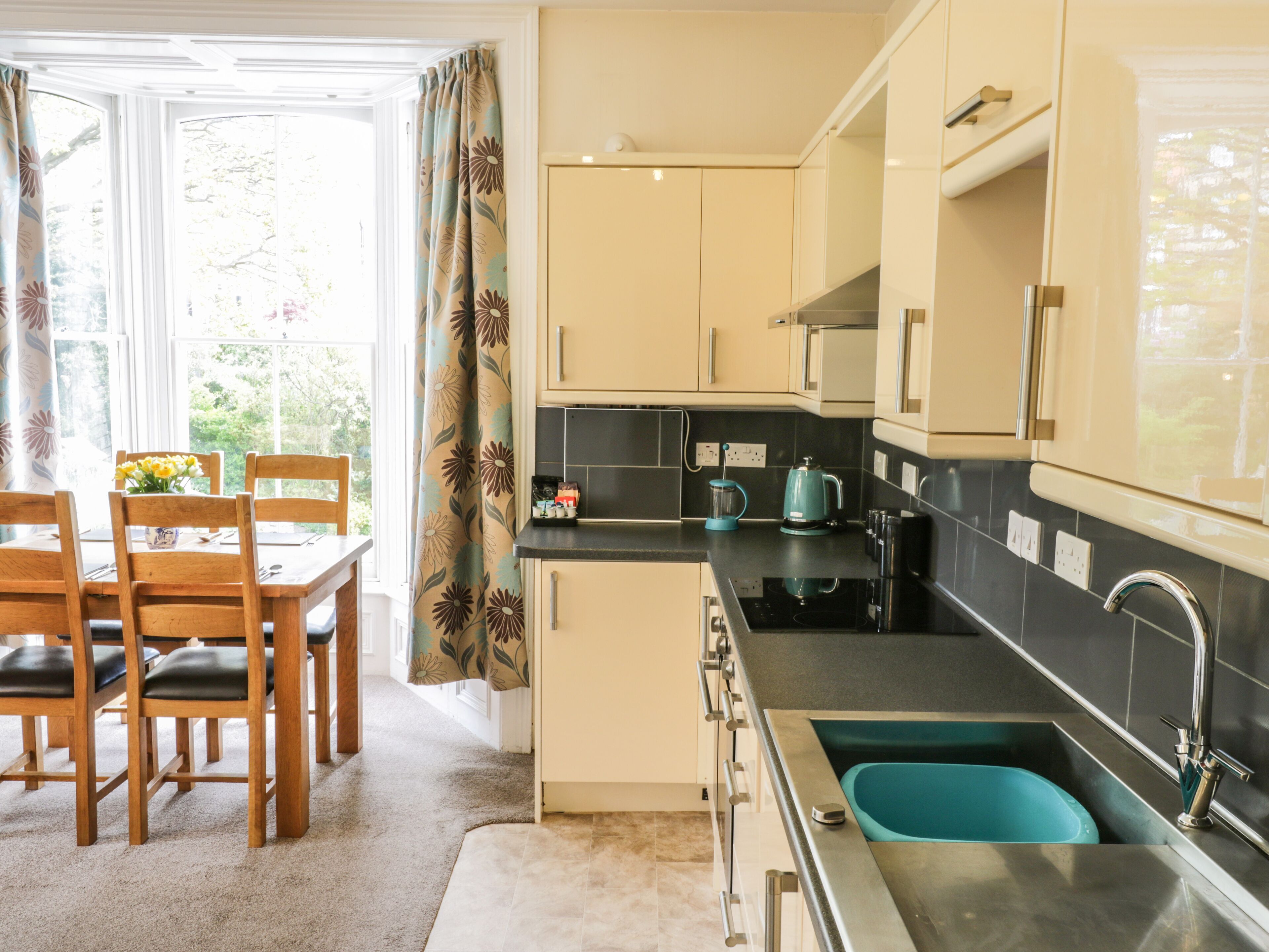 A modern kitchen with a sink, stove, and cabinets. There is a dining area with a table and chairs.