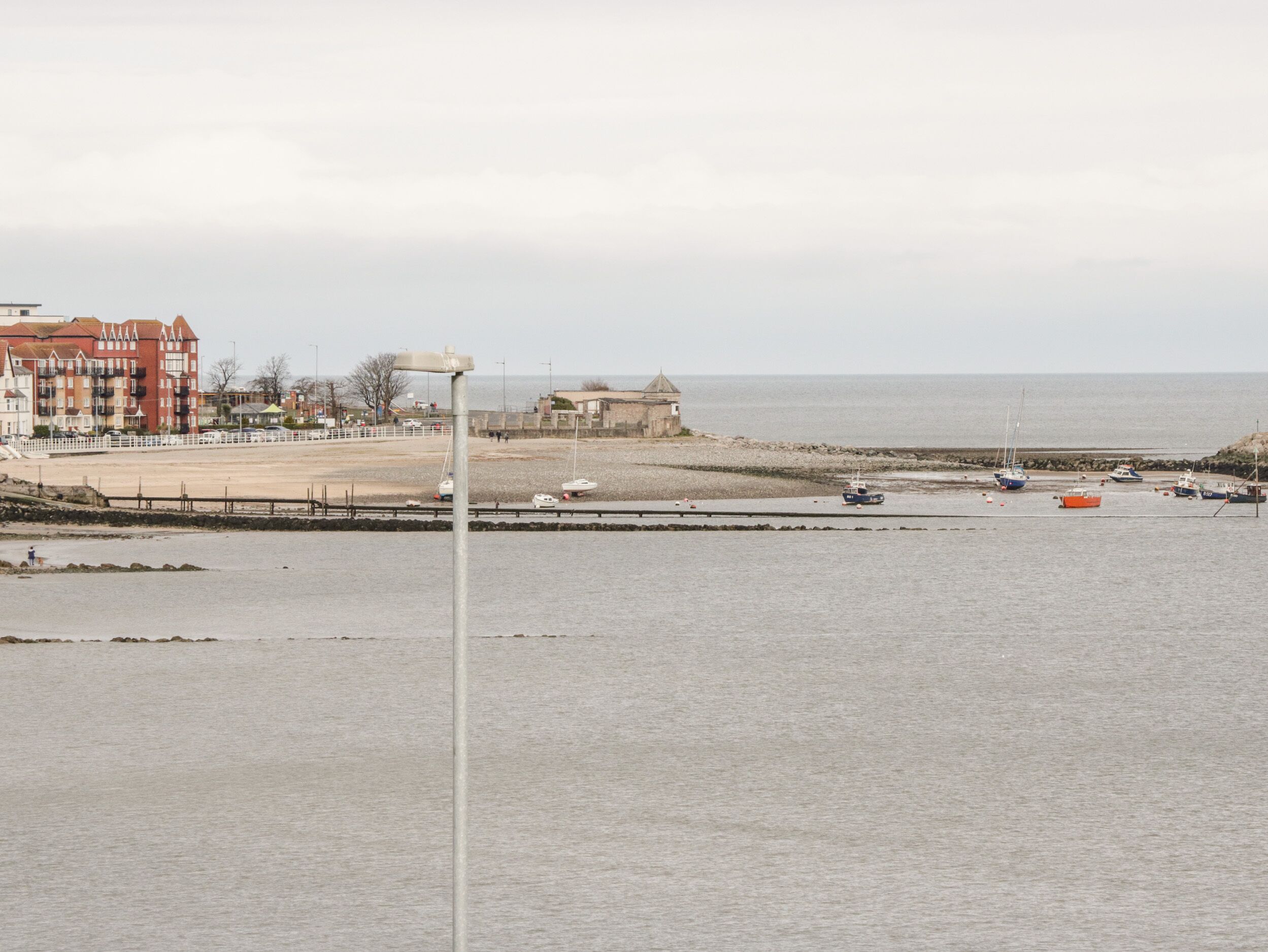 Zona costera con un paseo marítimo, un faro y varios barcos.