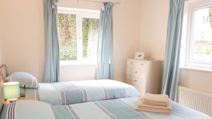 Un dormitorio con dos camas, una mesita de noche, un aparador y una ventana con cortinas.