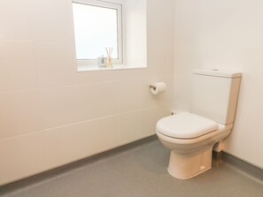 Une petite salle de bain moderne, équipée de toilettes, d’une fenêtre et d’un porte-rouleau de papier toilette.