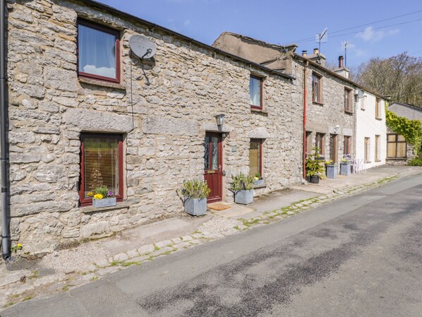 Une rangée de bâtiments en pierre, dotés de fenêtres et de portes, dont certains ont des volets, et une rue pavée devant.