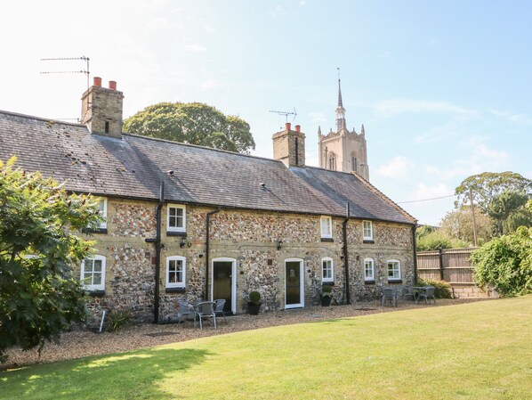 A stone house with a tiled roof, a front door, and a small garden with chairs and a table.