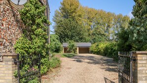 A gravel driveway leading to a building with a brick wall and a metal gate. - Flint Cottage (Swaffham)