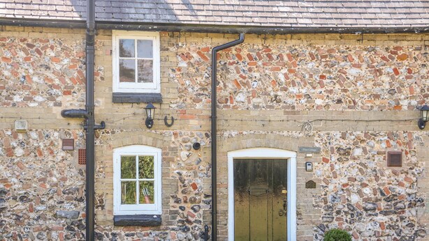 A stone building with a tiled roof, two windows, a door, and outdoor seating. - Flint Cottage (Swaffham)