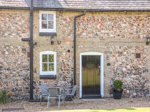 A stone building with a tiled roof, two windows, a door, and outdoor seating. - Flint Cottage (Swaffham)