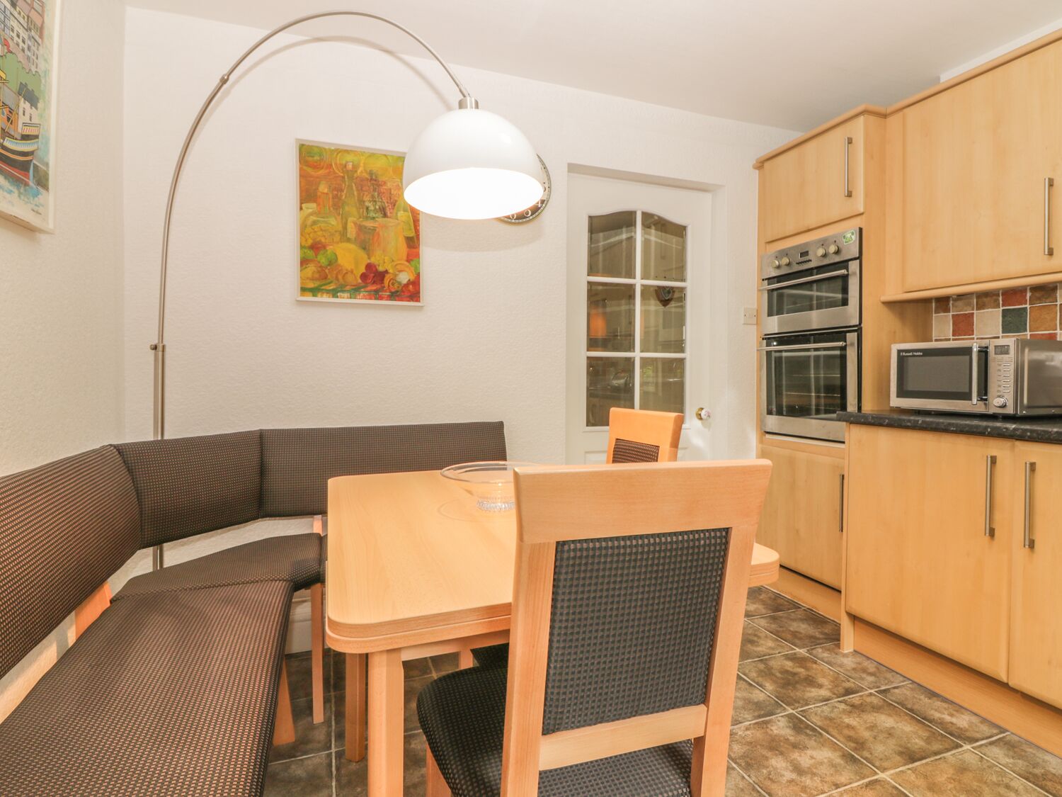 A compact kitchen with wooden cabinets, a microwave, and a dining area with a table and chairs.