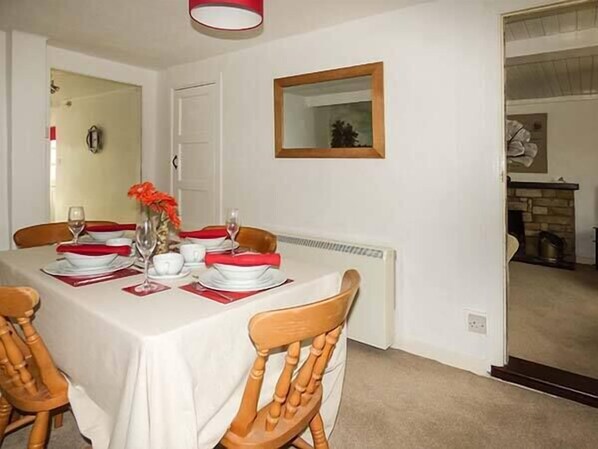 A dining area with a table set for four, white walls, a wooden chair, and a fireplace in the background. - Cobbler's Cottage (Norwich)
