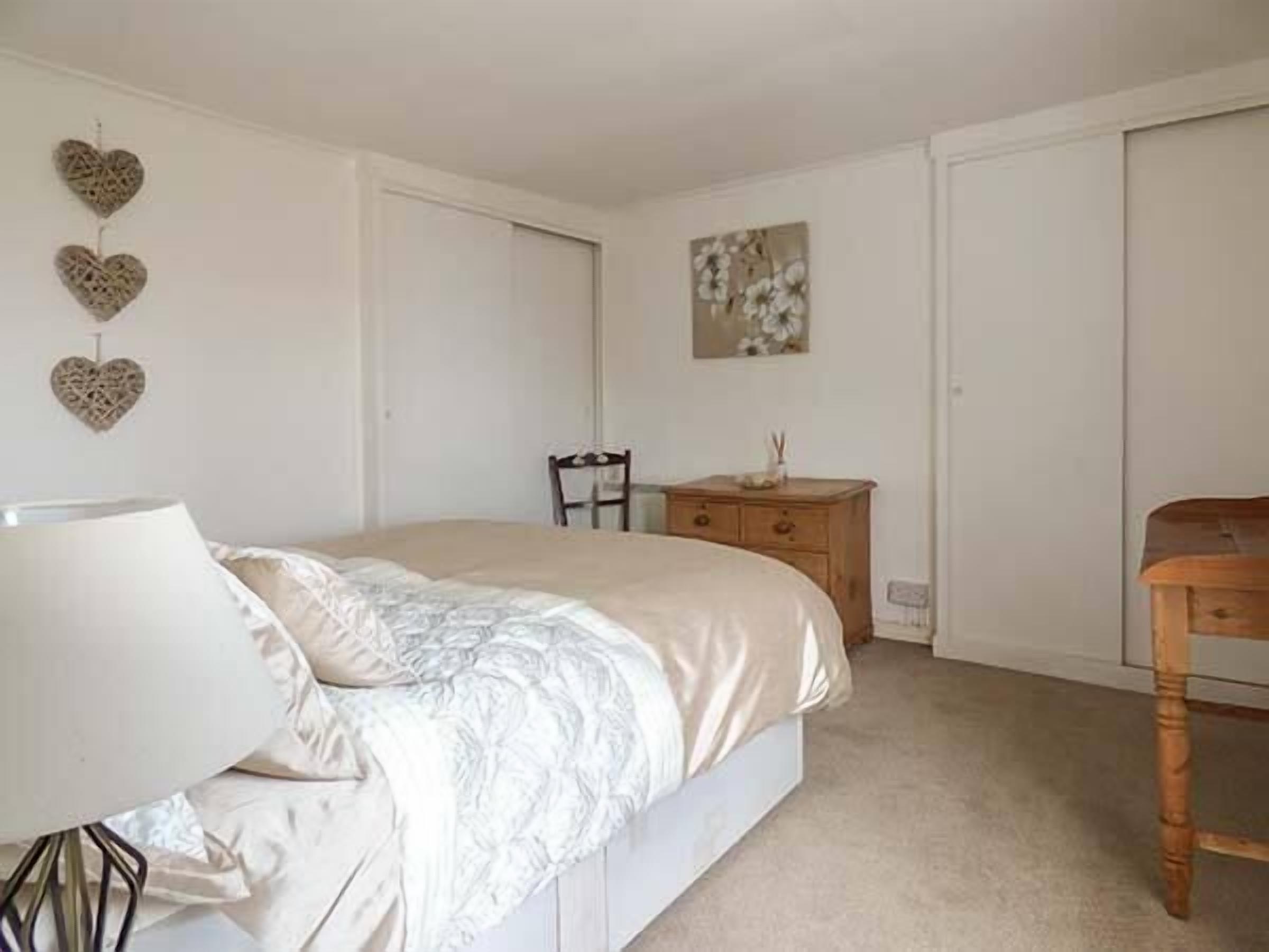 Un dormitorio con cama, cómoda, silla y lámpara de pared.