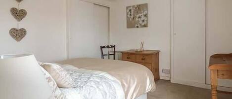 Un dormitorio con cama, cómoda, silla y lámpara de pared.