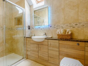 Bathroom features a glass-enclosed shower, large sink, and wooden vanity with towel storage.