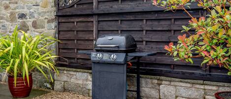 A barbecue grill in a garden area with stone walls and wooden lattice fence.