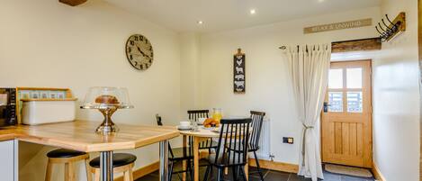 A cozy kitchen with a wooden ceiling, a round table with chairs, a clock, and a sign that reads "RELAX & UNWIND".