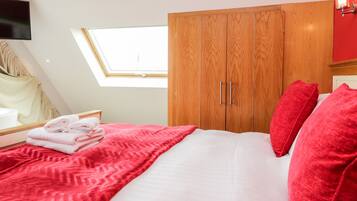 A bedroom with a bed, a wooden wardrobe, a skylight, and a television on the wall.