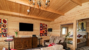 A cozy log cabin interior with a leather sofa, wooden walls, a television, and artwork.