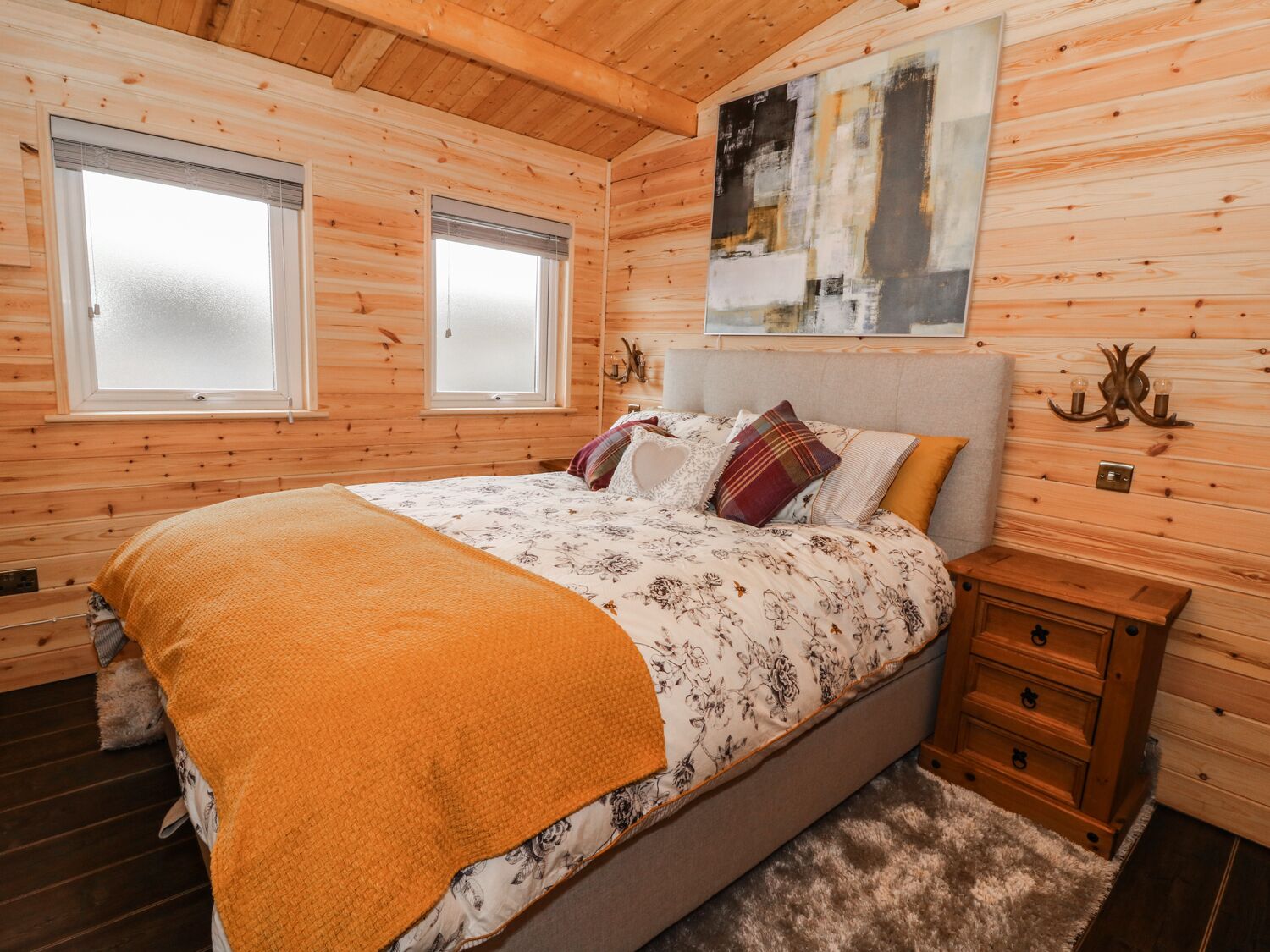 Camera da letto in una baita di legno con un letto, due finestre, un quadro e un comodino.