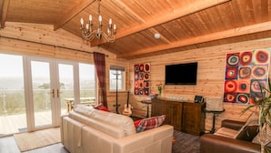 A cozy living room with a sofa, a coffee table, and a TV mounted on the wall. There is a balcony with a view outside.