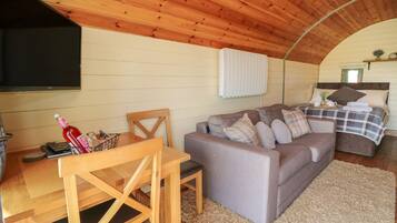A cozy cabin interior with a wooden ceiling, a sofa, a dining table, and a TV.