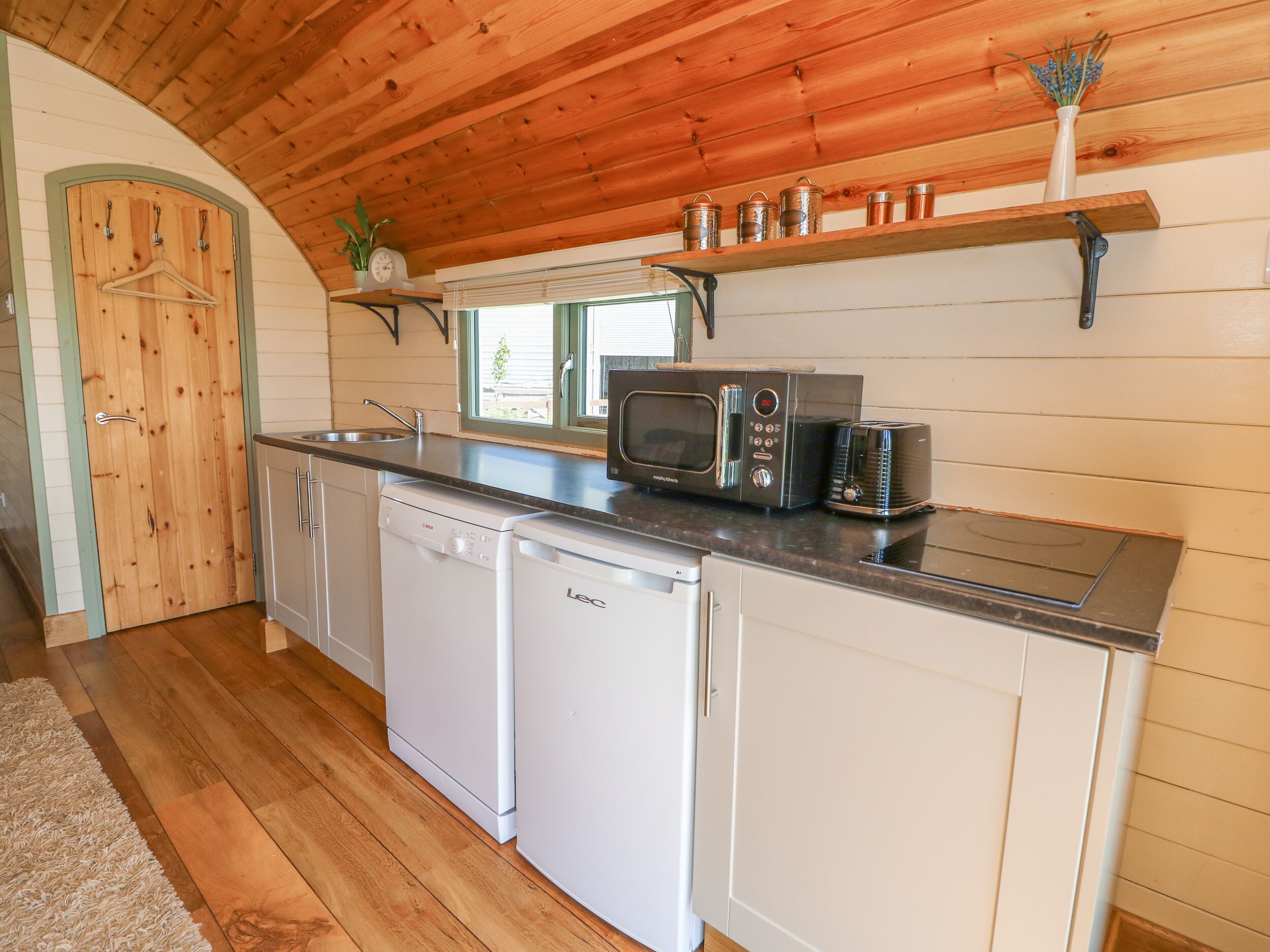 A compact kitchen with wooden cabinets, a dishwasher, a microwave, and a toaster.