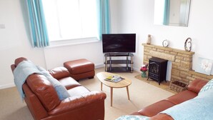 A living room with a brown leather sofa, a coffee table, a flat-screen TV, a fireplace, and a stone wall.