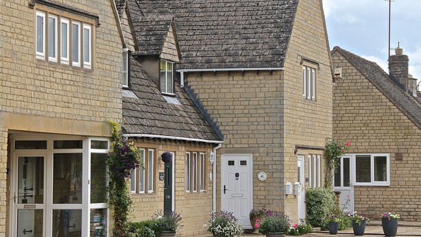 A traditional stone building with a steeply pitched roof, a white door, and multiple windows.