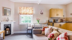 A cozy living room with a sofa, a fireplace, a dining table, and a kitchen area with wooden cabinets.