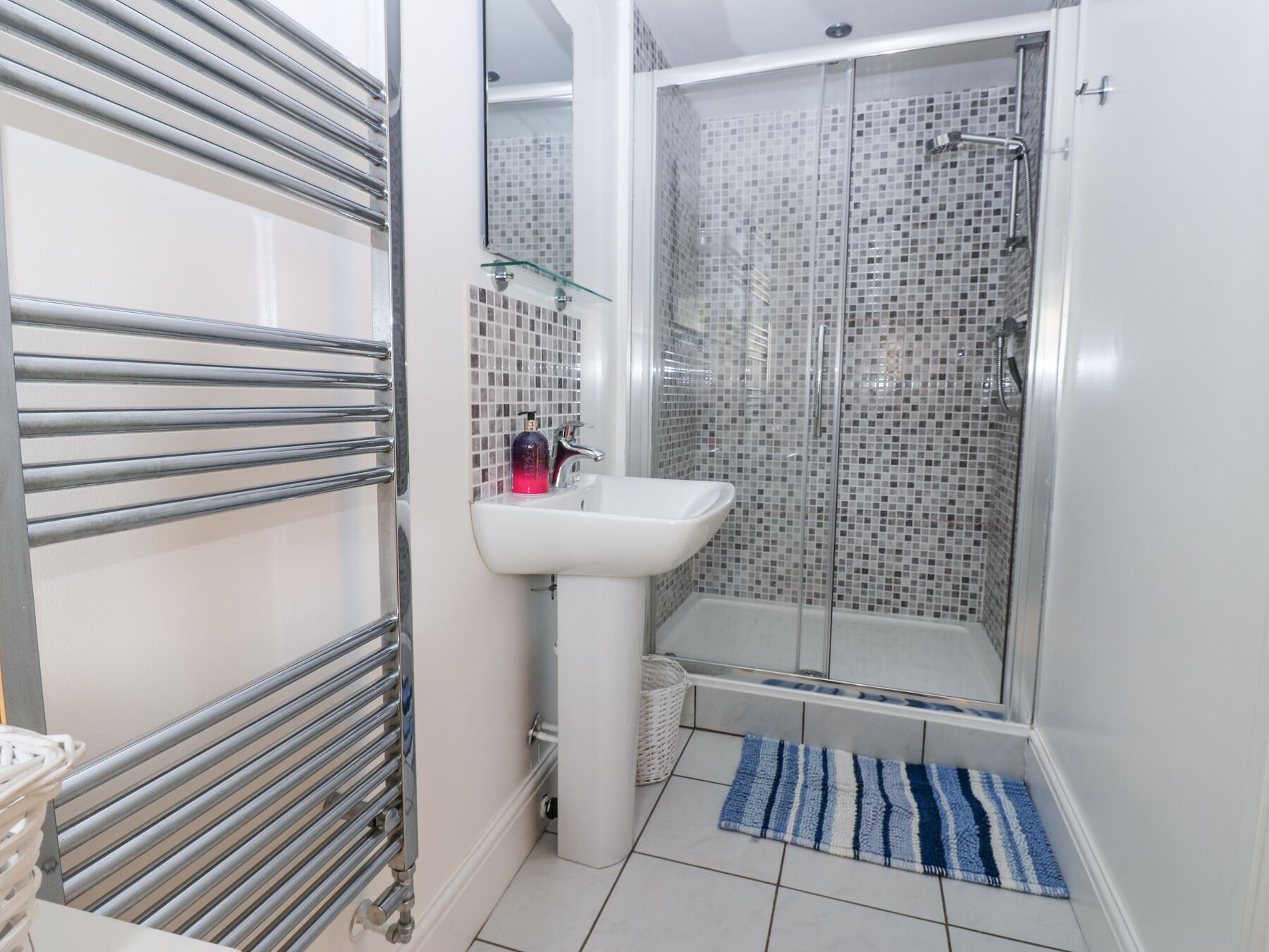 A bathroom with a glass shower enclosure, a white sink, and a towel rack.