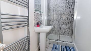 A bathroom with a glass shower enclosure, a white sink, and a towel rack.