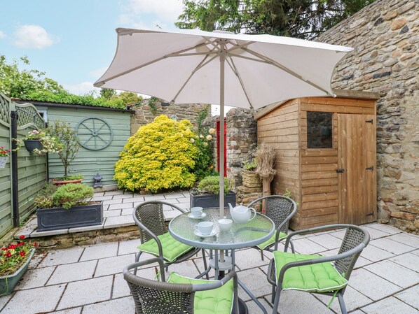 A patio with a round table, four chairs, a white umbrella, and a wooden shed. - Mill Cottage (Bishop Auckland)